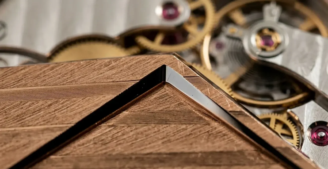 Vue macro d'un angle rentrant poli main sur un pont de mouvement horloger en or rose avec reflets lumineux