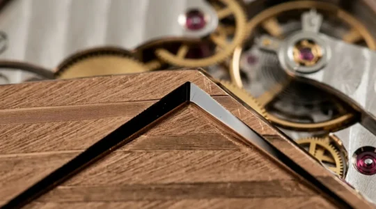 Vue macro d'un angle rentrant poli main sur un pont de mouvement horloger en or rose avec reflets lumineux