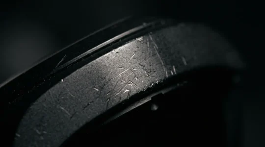 Détail macro d'une montre en céramique noire montrant des rayures superficielles sous lumière rasante