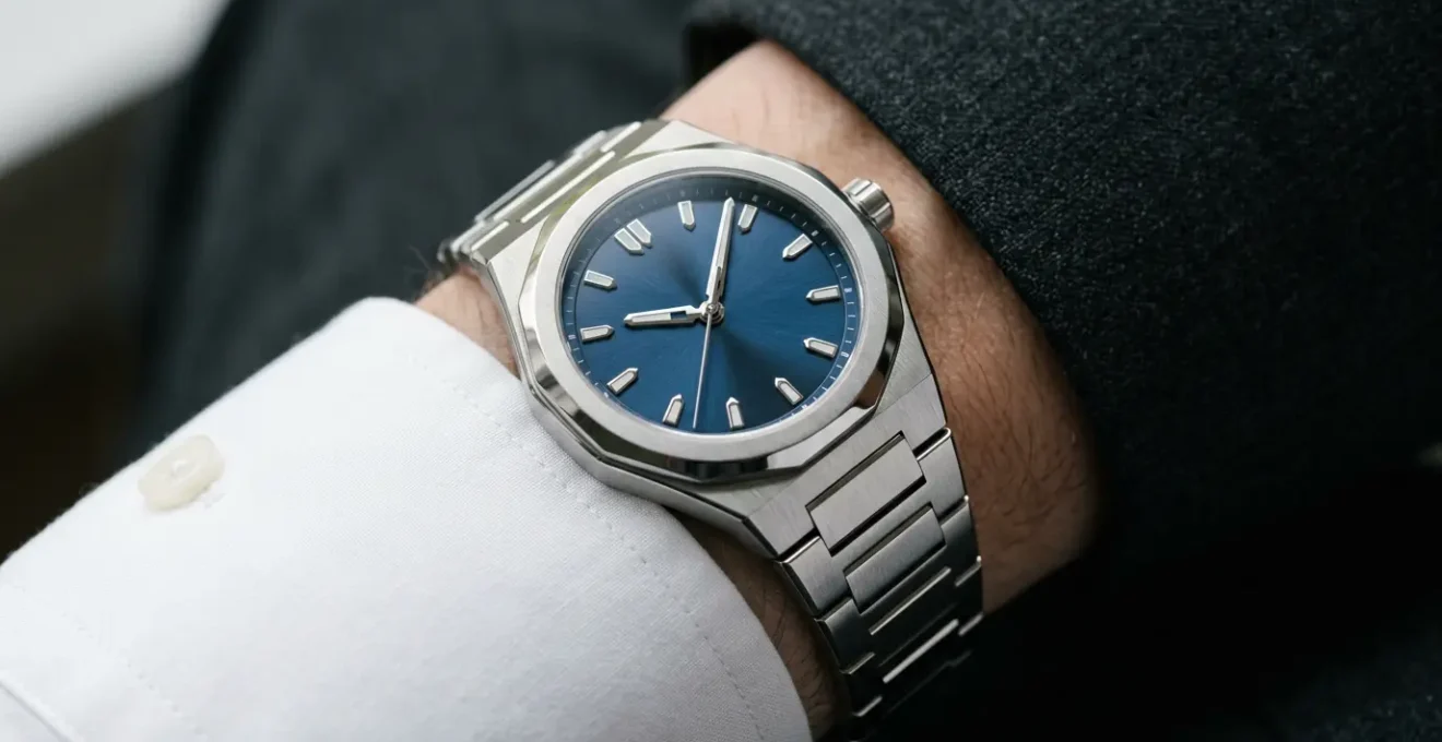 Montre de sport en acier avec bracelet intégré posée élégamment sur une manche de chemise blanche sous une veste de costume anthracite