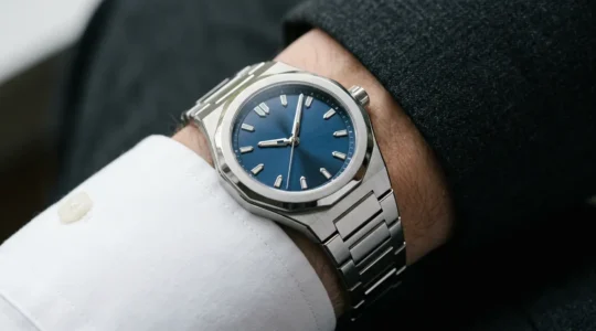 Montre de sport en acier avec bracelet intégré posée élégamment sur une manche de chemise blanche sous une veste de costume anthracite