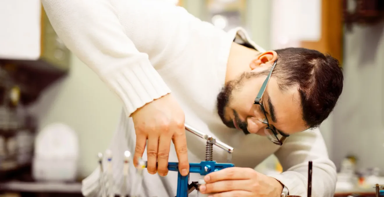 Un horloger place une montre dans un caisson de test d'étanchéité en surpression, équipé d'une jauge de pression, dans un atelier de manufacture.